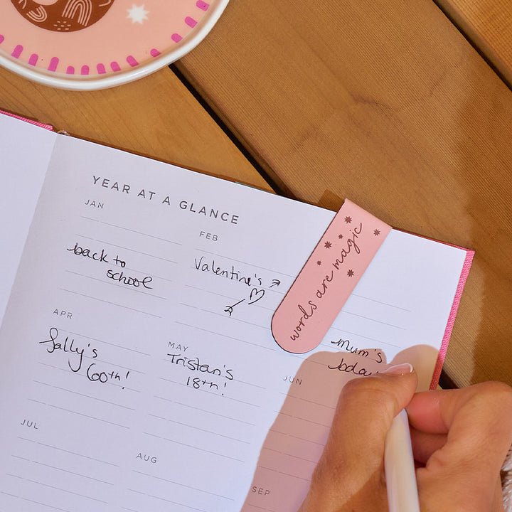 Handwritten planner with a pink bookmark on a wooden surface