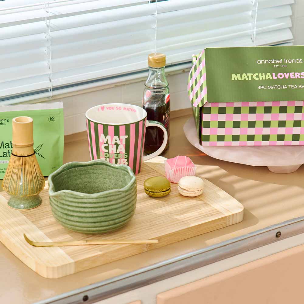 Matcha tea set with a green bowl, pink mug, and matcha powder container on a wooden tray.