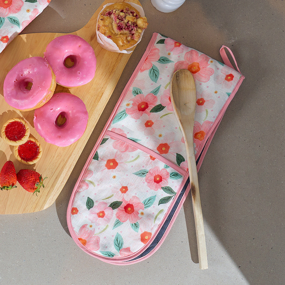 Floral oven mitt and pot holder with pink donuts and strawberries on a wooden board.