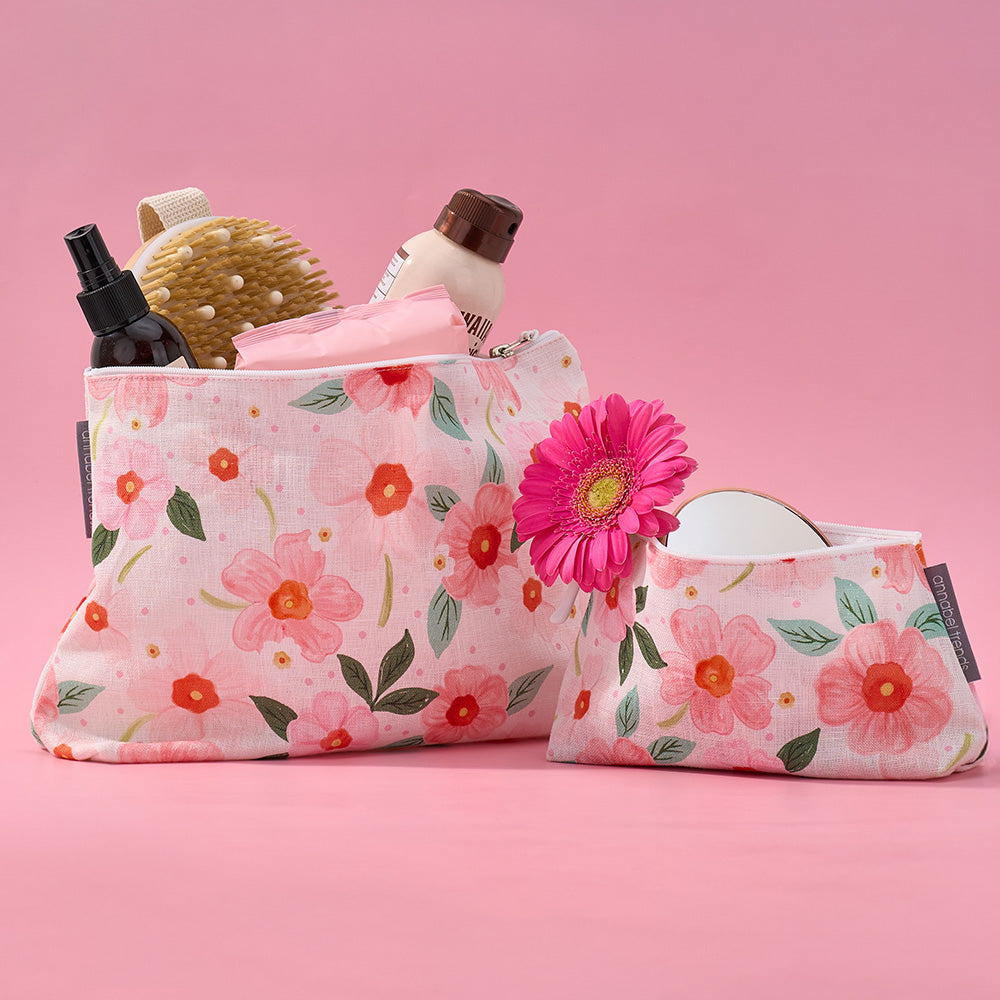 Floral-patterned makeup bags with cosmetic items on a pink background
