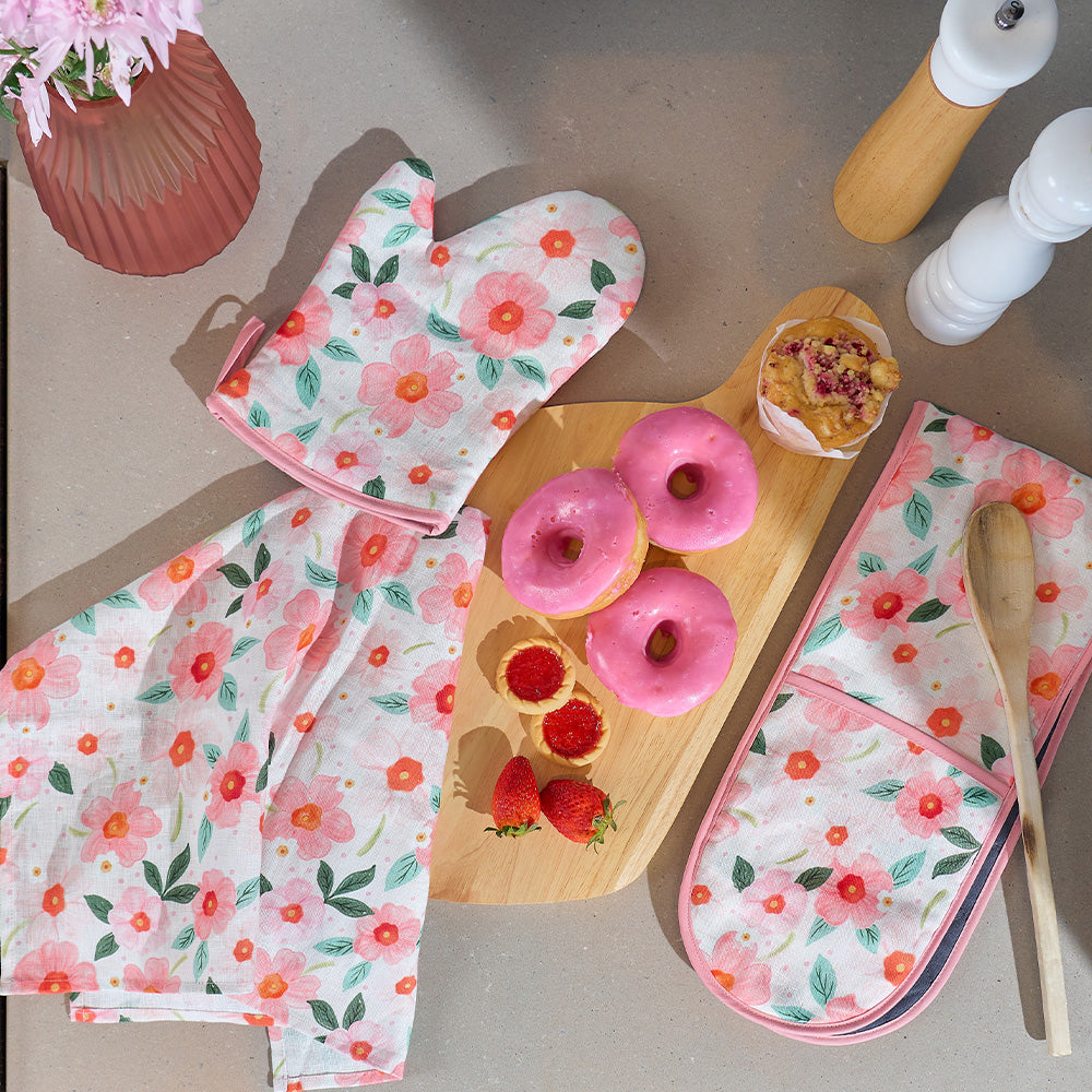 Floral oven mitts and pot holder with pink donuts on a wooden board.
