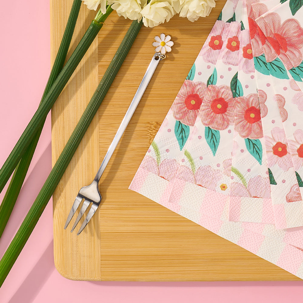 Floral-patterned napkin, fork, and flowers on a wooden board with a pink background