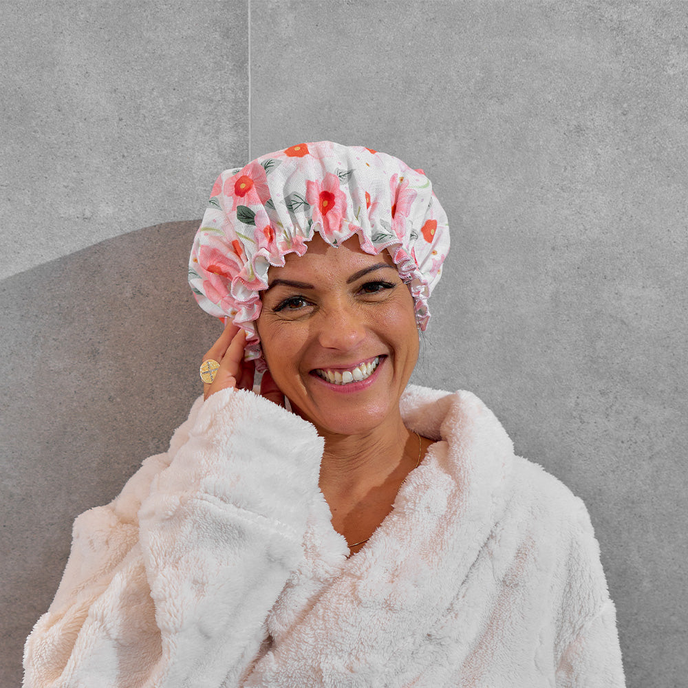 Woman wearing a floral shower cap and white robe against a gray background