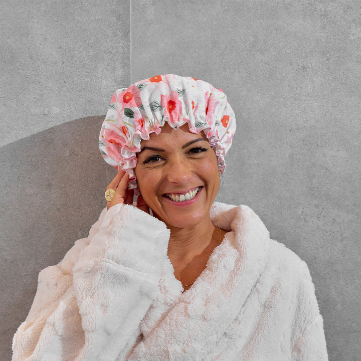 Woman wearing a floral shower cap and white robe against a gray background