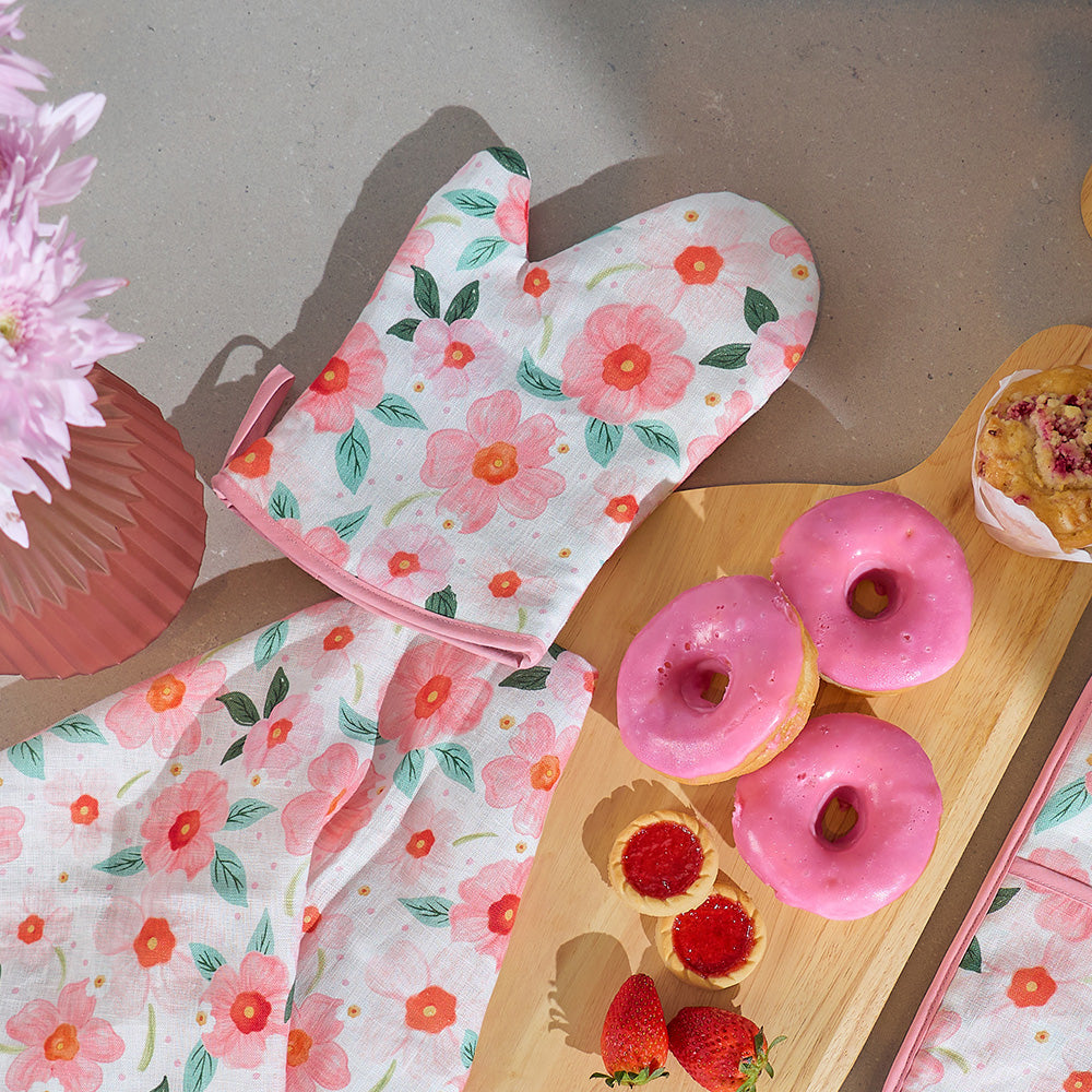 Floral-patterned oven mitt on a table with pink donuts and strawberries.