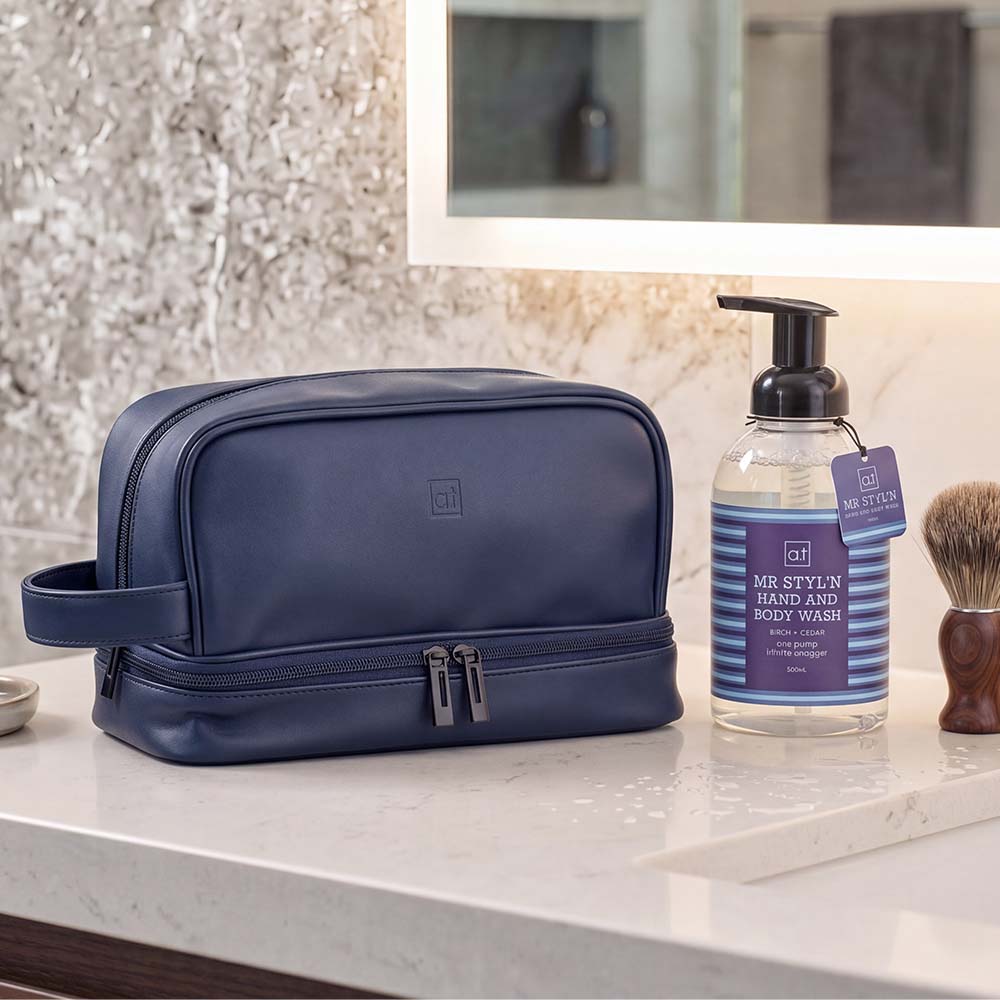 Blue toiletry bag on a bathroom counter with hand and body wash and a brush.