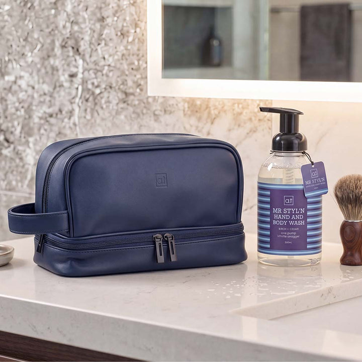 Blue toiletry bag on a bathroom counter with hand and body wash and a brush.
