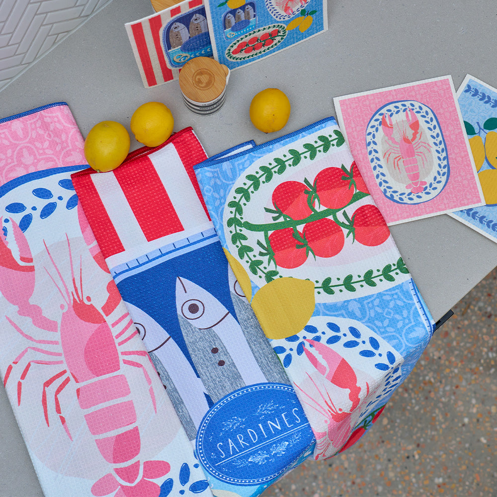 Colorful kitchen towels with seafood and tomato designs on a gray surface.