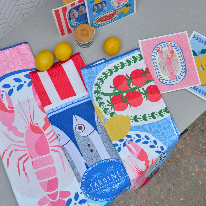 Colorful kitchen towels with seafood and tomato designs on a gray surface.