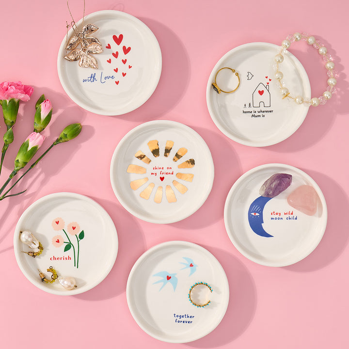 Set of small decorative plates with various designs and text on a pink background