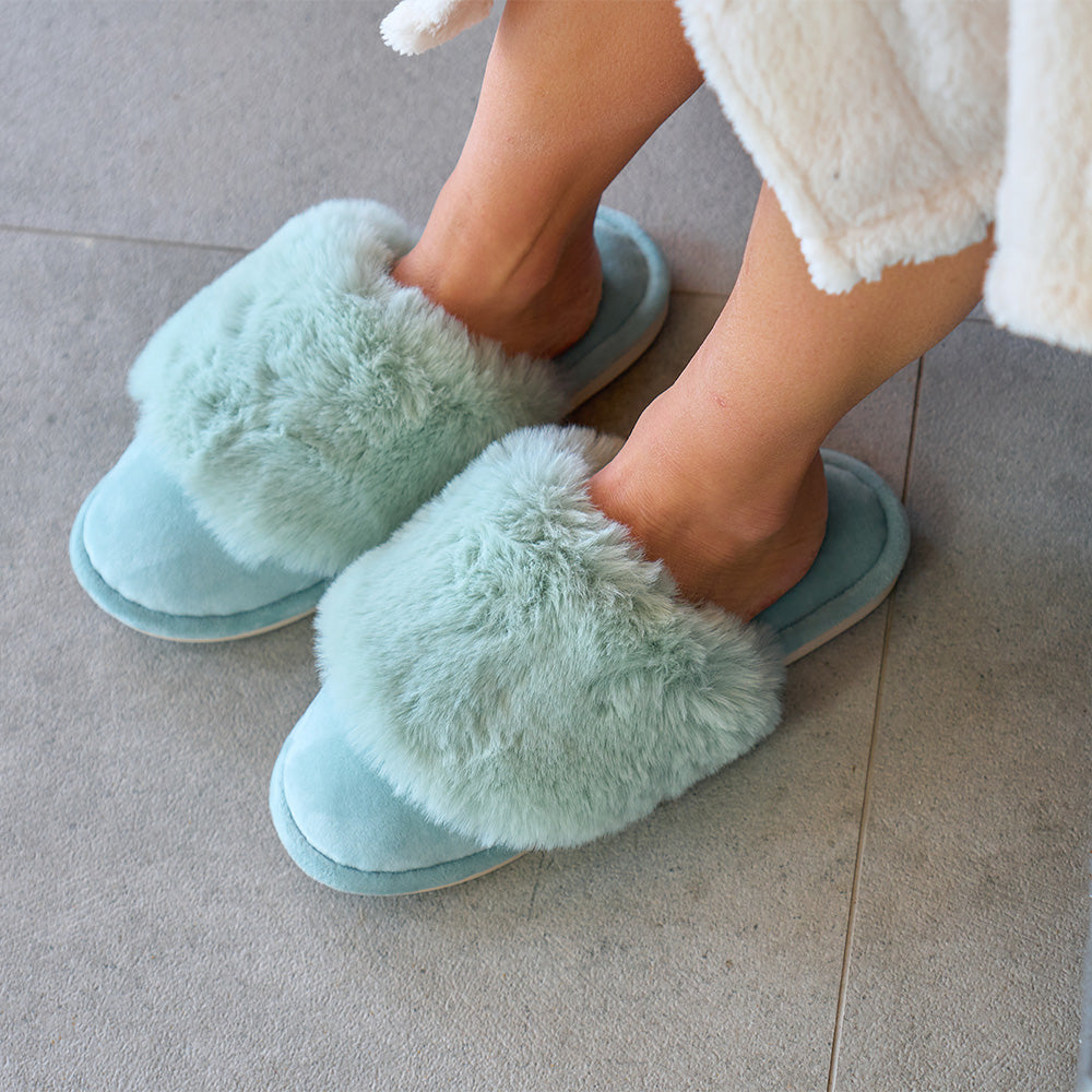 Person wearing mist green fluffy slippers on a tiled floor