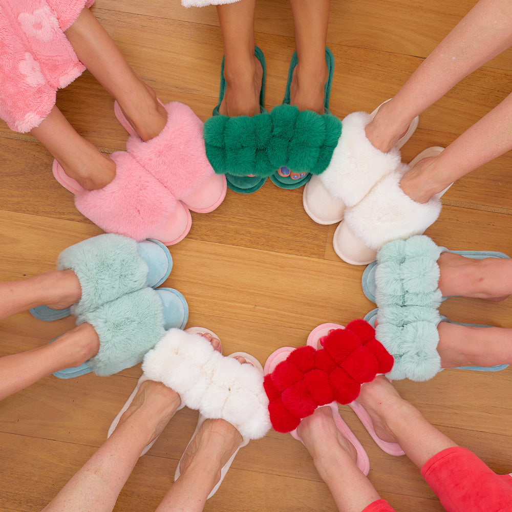 Colorful fluffy slippers worn by multiple people on a wooden floor.