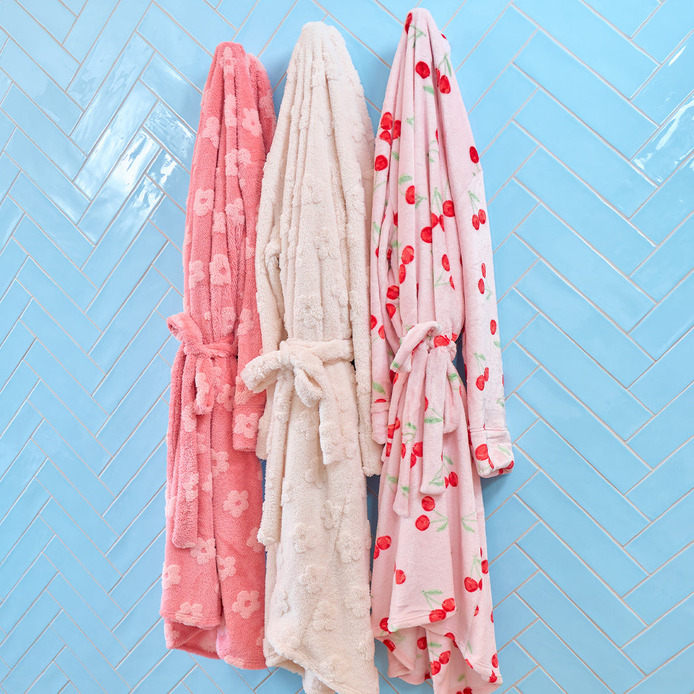 Three bathrobes hanging against a blue tiled wall.