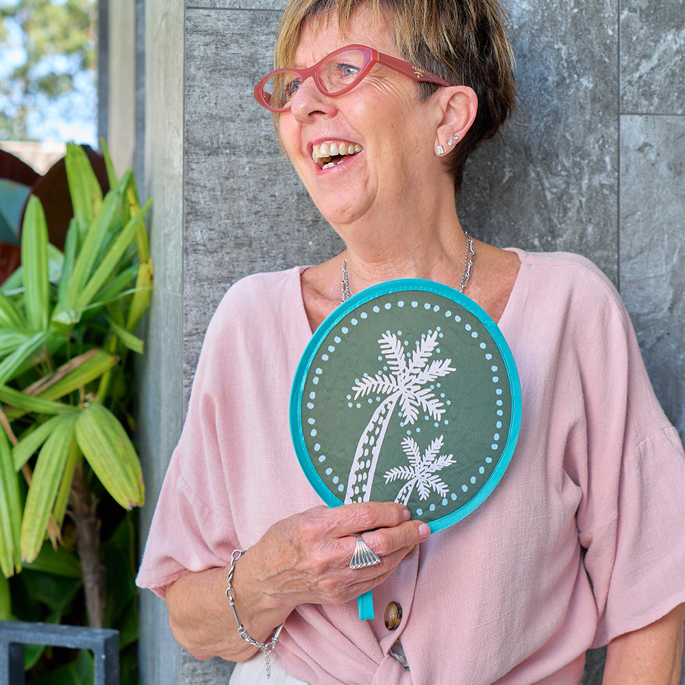 Woman holding a circular twist fan with a palm tree design outdoors
