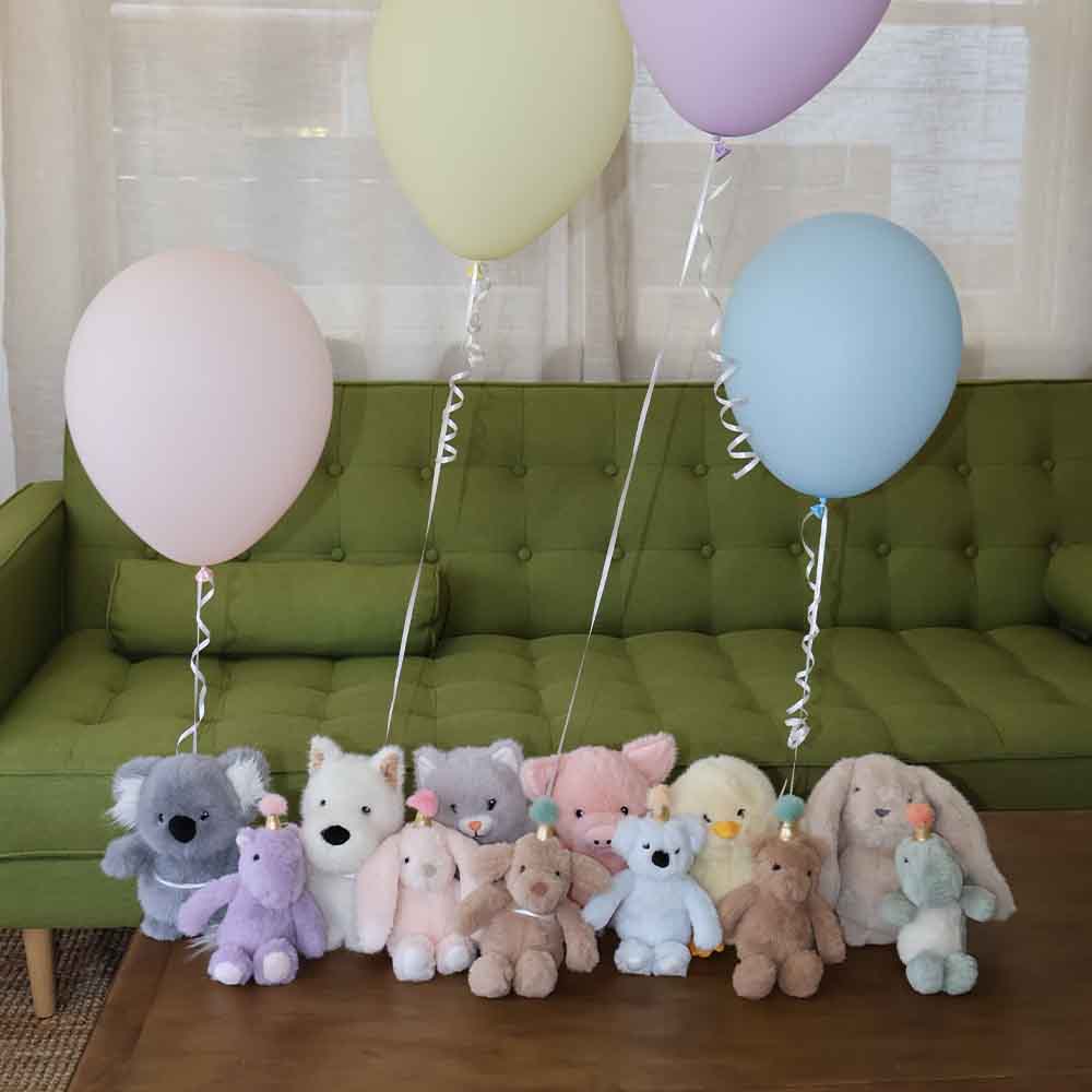 Colorful balloons and soft toys on a wooden table with a green couch in the background.