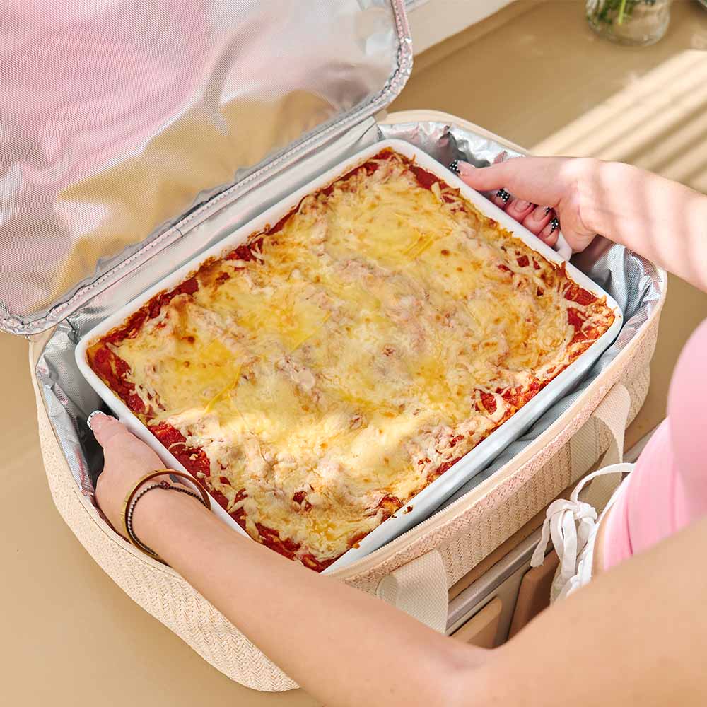 Person holding a thermos container with a lasagna inside on a wooden surface.