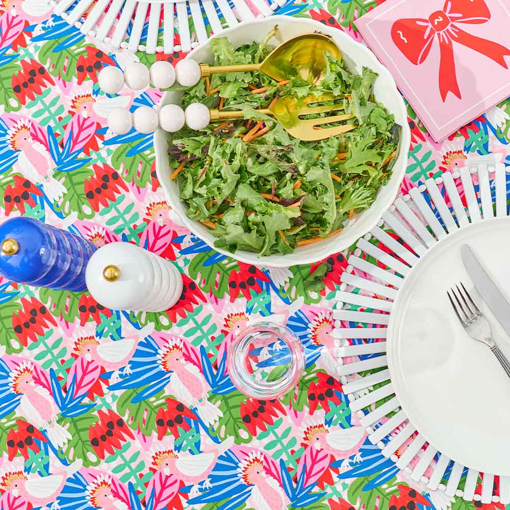 Colorful table setting with a bowl of salad, cutlery, and decorative elements on a patterned tablecloth.