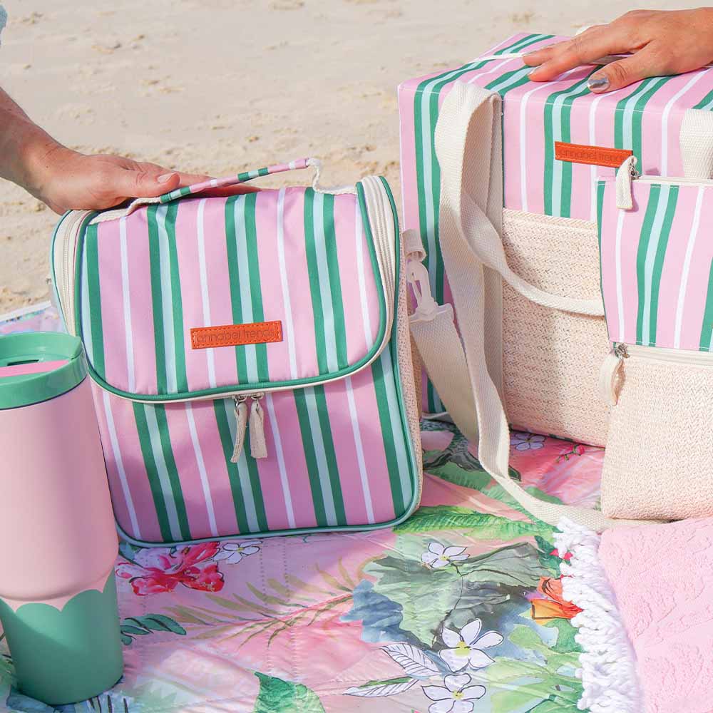 Pink and green striped bags on a floral blanket with a person's hand holding one of them.