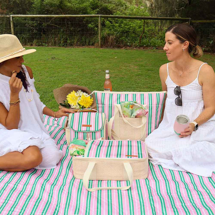 Two women sitting on a striped blanket with picnic items in an outdoor setting.