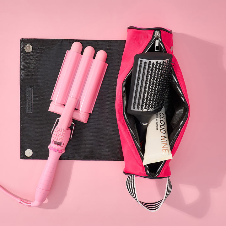 Pink hair curling iron and brush set with a pink case on a pink background