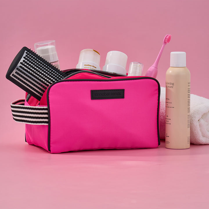Pink toiletry bag with hairbrush, bottles, and toothbrush on a pink background