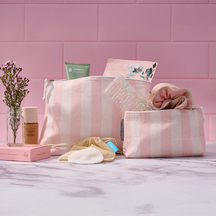 Pink striped toiletry bag with cosmetic items on a pink tiled background