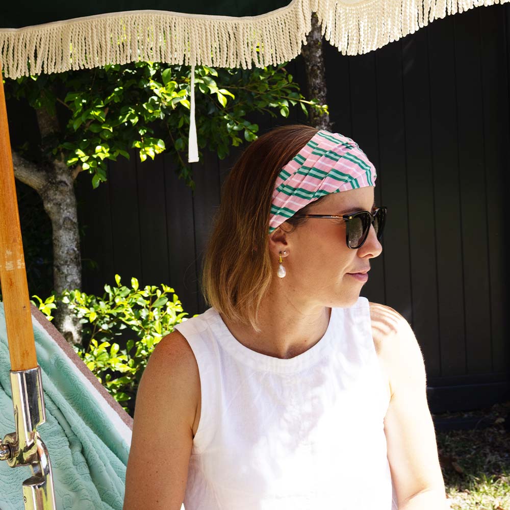 Woman wearing a pink and green headband sitting in a hammock with a garden background