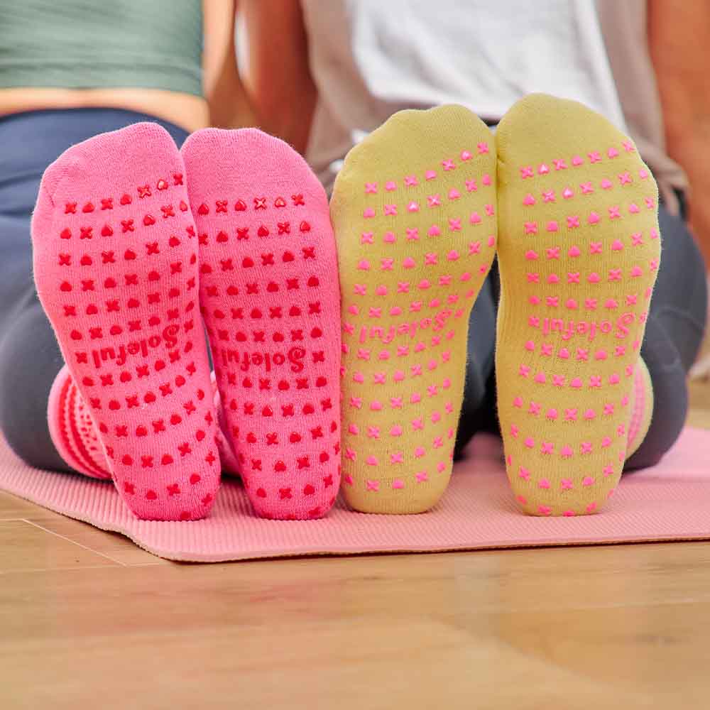 Pink and green yoga socks with textured sole on a pink mat.