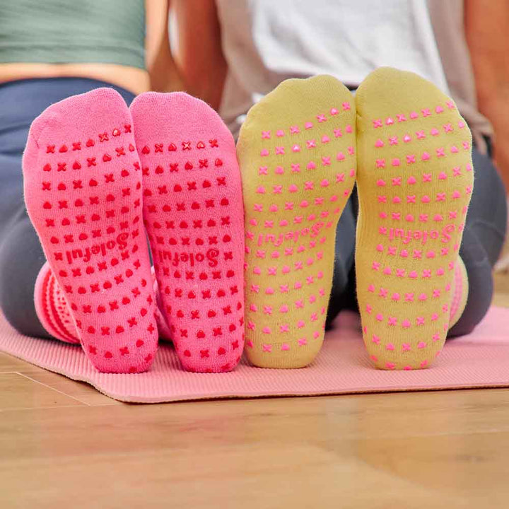Pink and green yoga socks with textured sole on a pink mat.