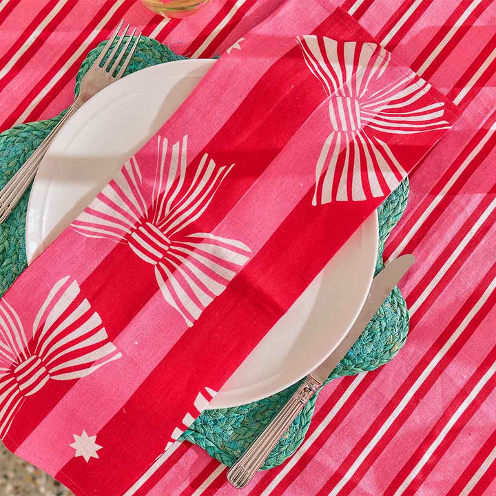 red and pink stripe cloth napkin with white printed bows sitting on a red stripe tablecloth