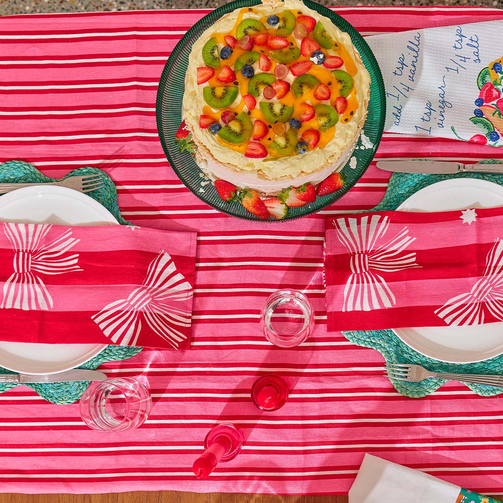 Fruit tart on a red and white striped tablecloth with cutlery and plates.
