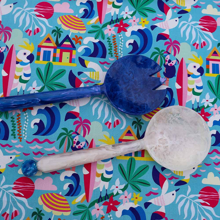 Two spoons on a colorful patterned fabric with beach-themed designs.