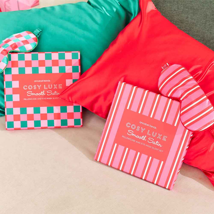 Two boxes of Cosy Luxe Smooth Satin products on a bed with red and green bedding.