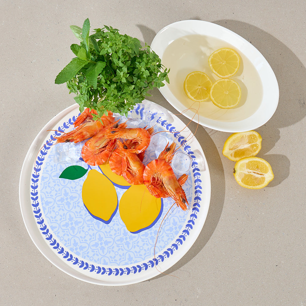Platter of cooked prawns with lemons and herbs on a neutral background
