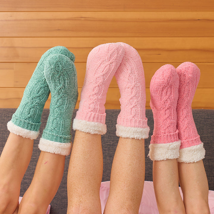 Three pairs of knitted chenille sherpa lined socks worn by people against a wooden background.