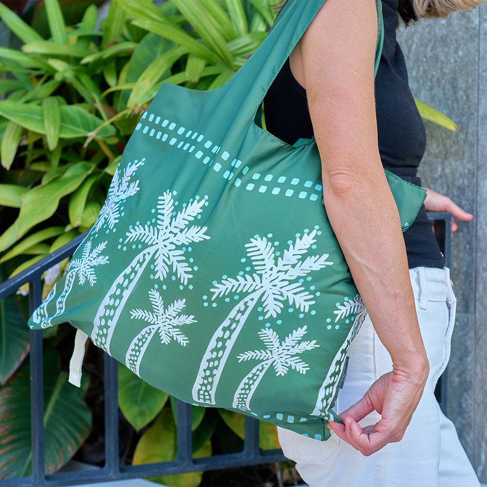 Green tote bag with white floral patterns held by a person outdoors.