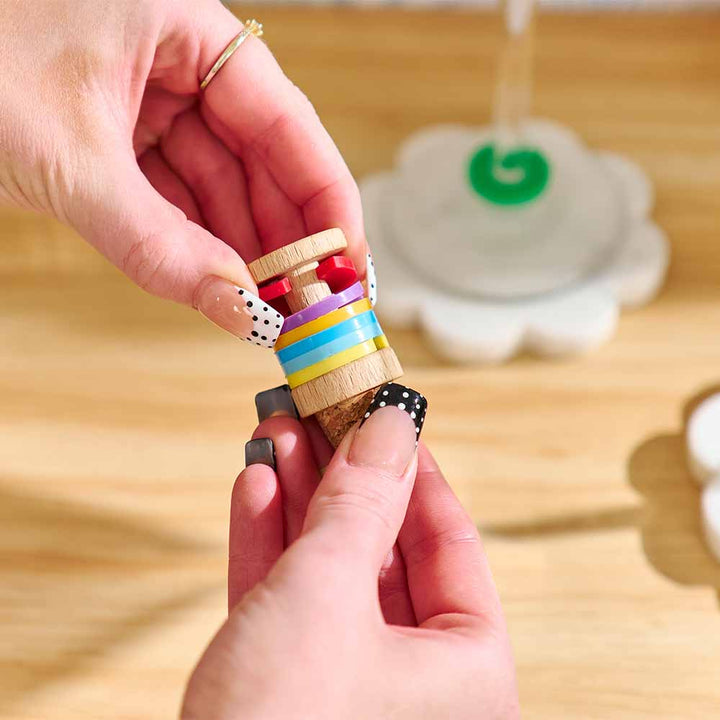 Small wooden toy with colorful stripes held by a hand on a wooden surface.