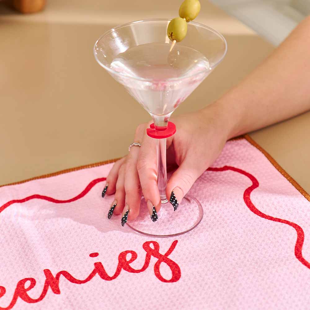 Hand holding a martini glass with olives on a pink towel with red text