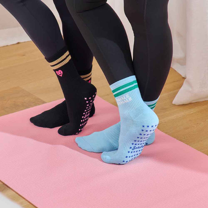 Two pairs of legs wearing black leggings and colorful socks on a pink yoga mat.