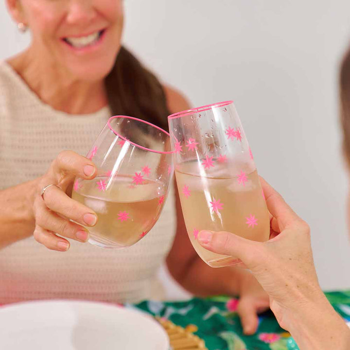 Two people holding glasses of pink champagne with star decorations against a neutral background