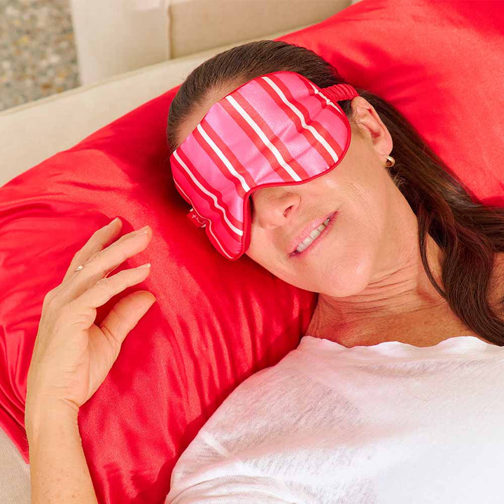 Woman wearing a pink striped eye mask on a red pillow