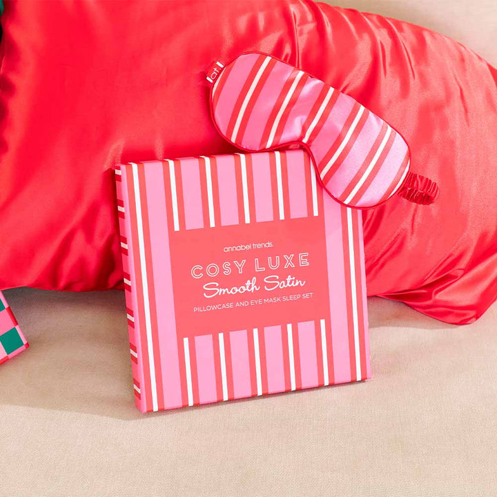 Pink striped pillowcase and eye mask set with 'Cosy Luxe' branding on a beige surface.