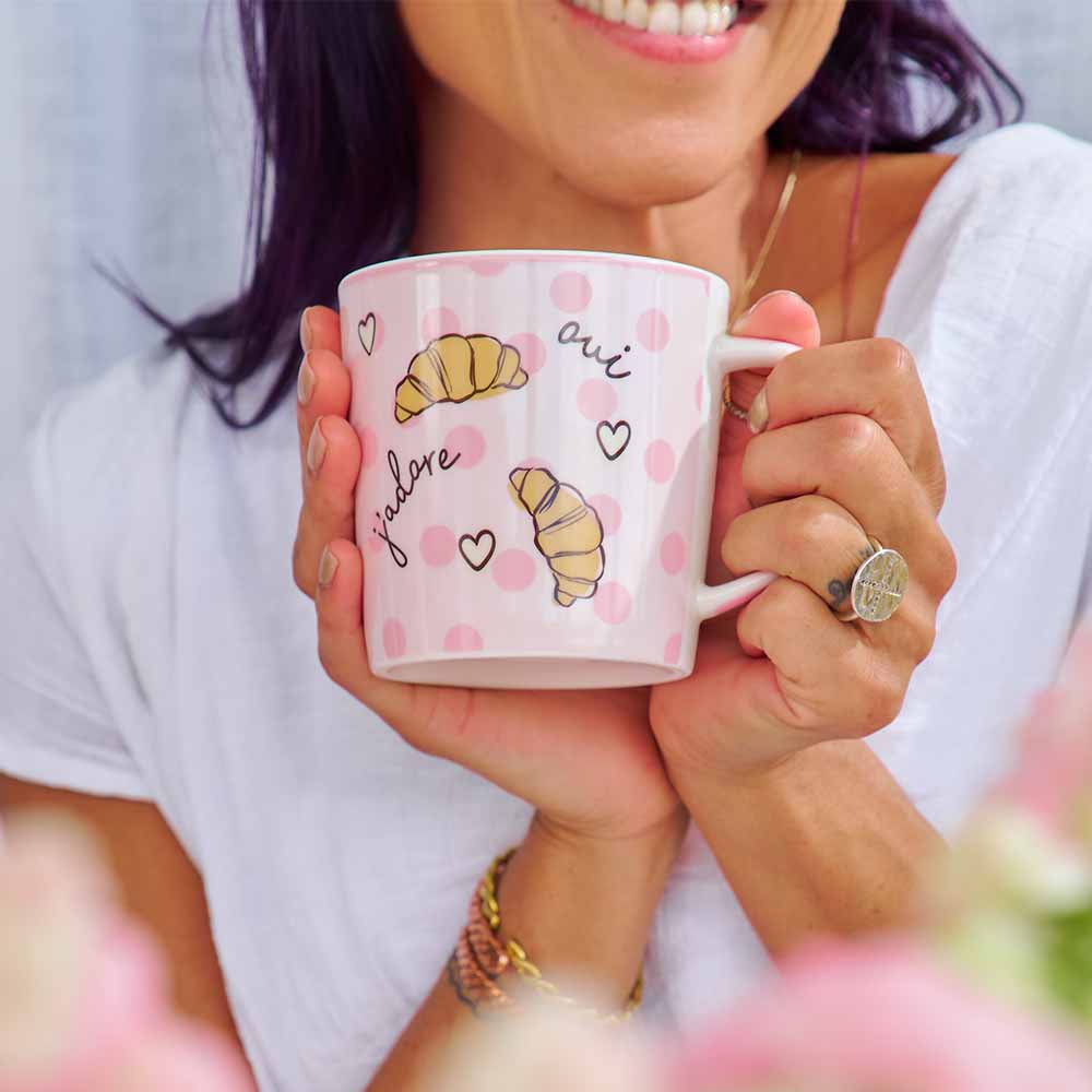 Person holding a pink mug with croissant designs and the word 'love'.