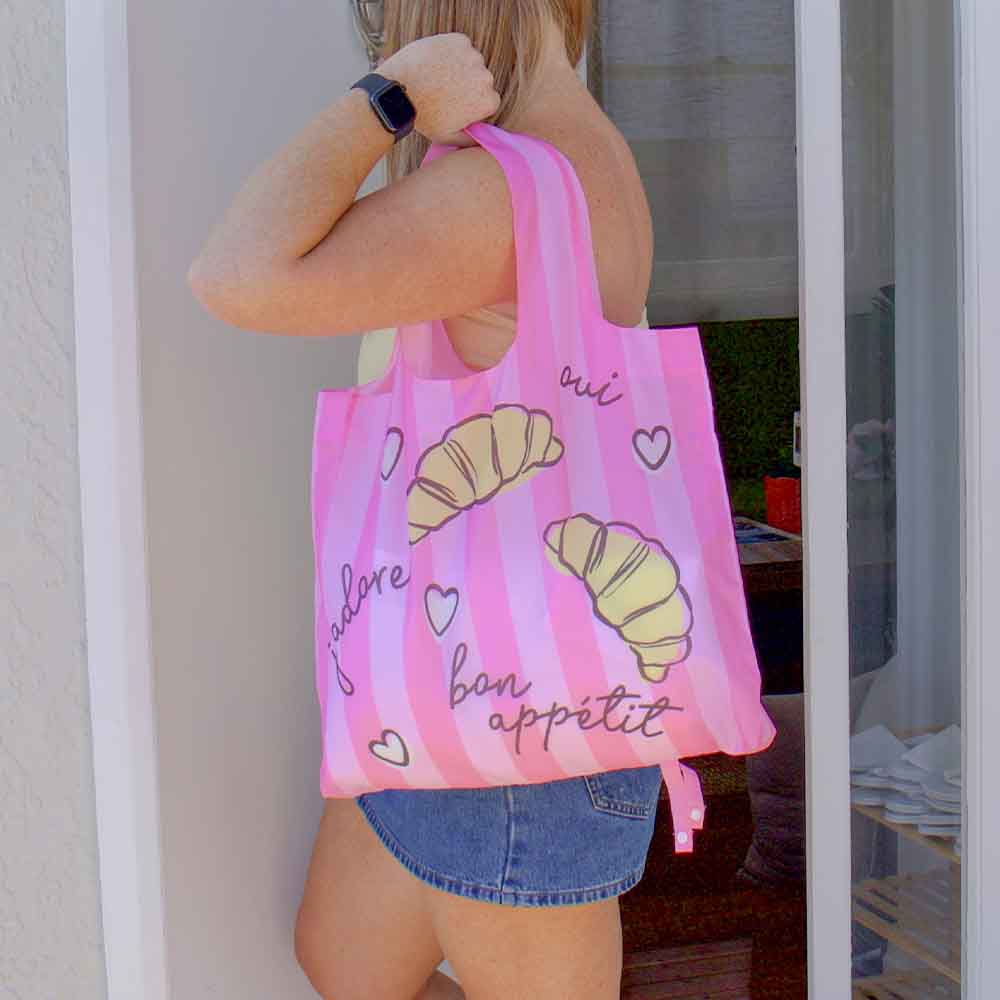 Person holding a pink tote bag with croissant designs and text.
