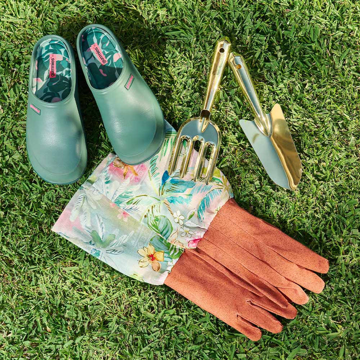 Gardening tools and accessories including green shoes, gloves, and a trowel on grass.