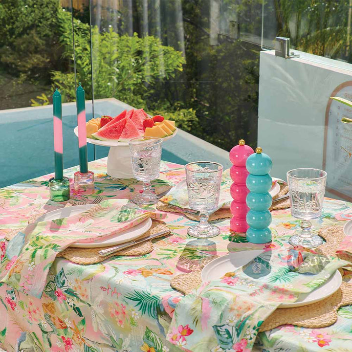 Outdoor table setting with colorful candles, watermelon, and glasses on a floral tablecloth.