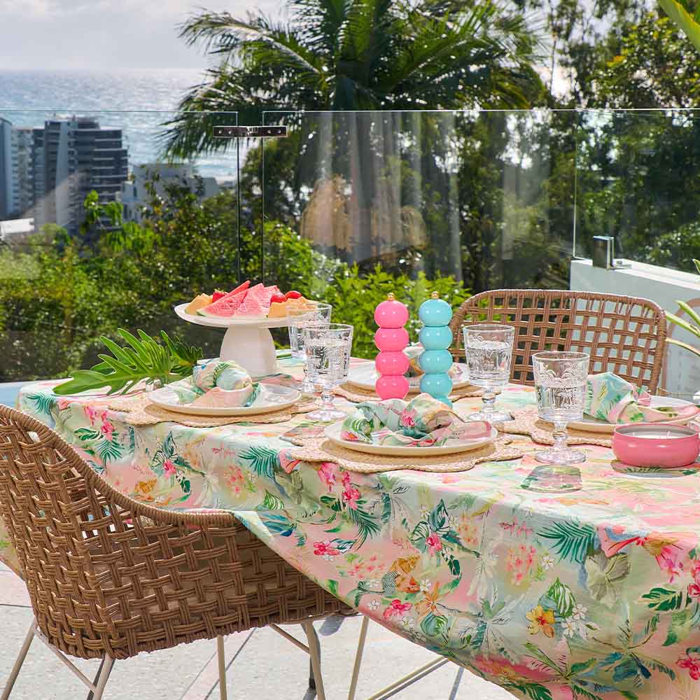 Outdoor table setting with floral tablecloth, colorful decor, and ocean view.