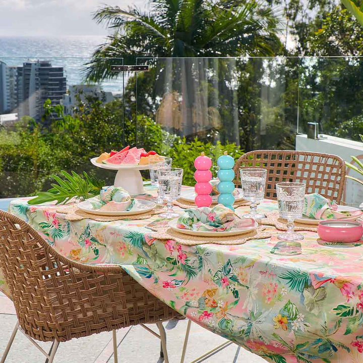 Outdoor table setting with floral tablecloth, colorful decor, and ocean view.