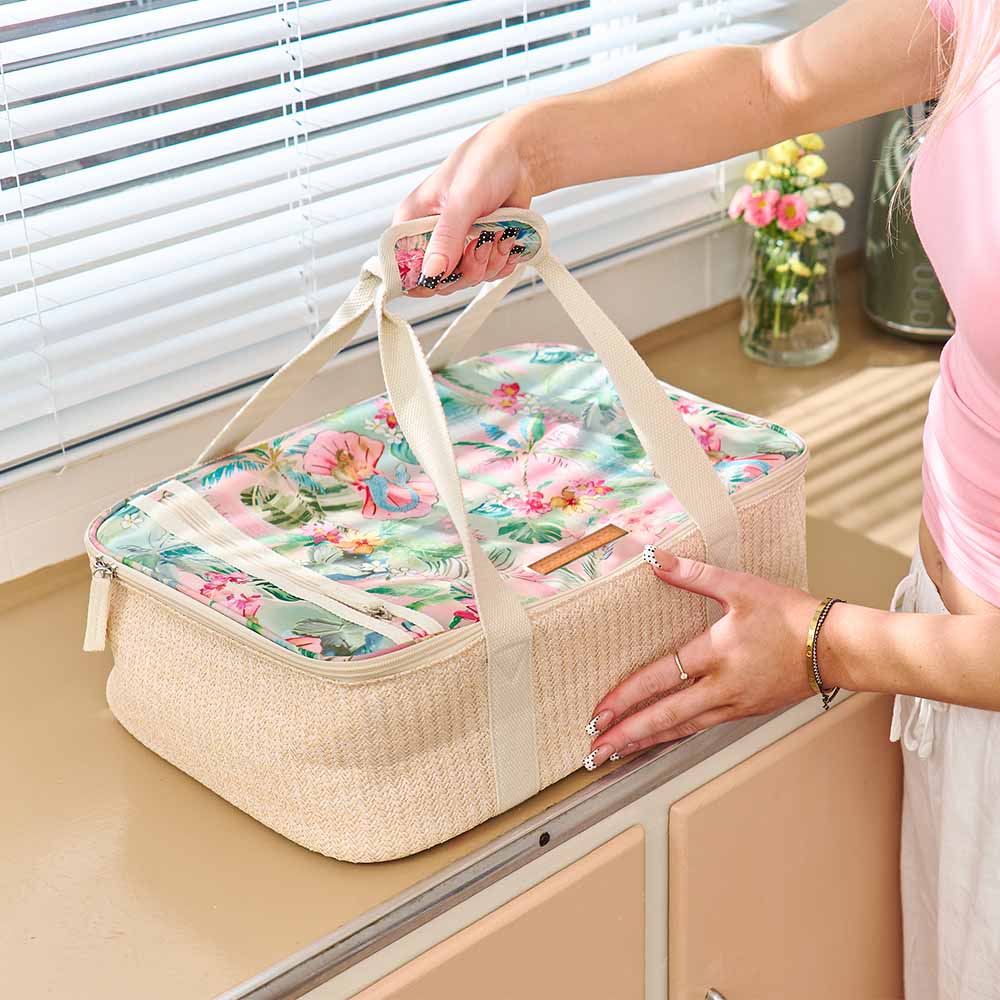 Floral-patterned picnic basket with beige handle held by a person.
