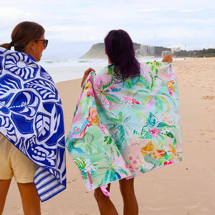 Two people on a beach with patterned towels draped over their shoulders.